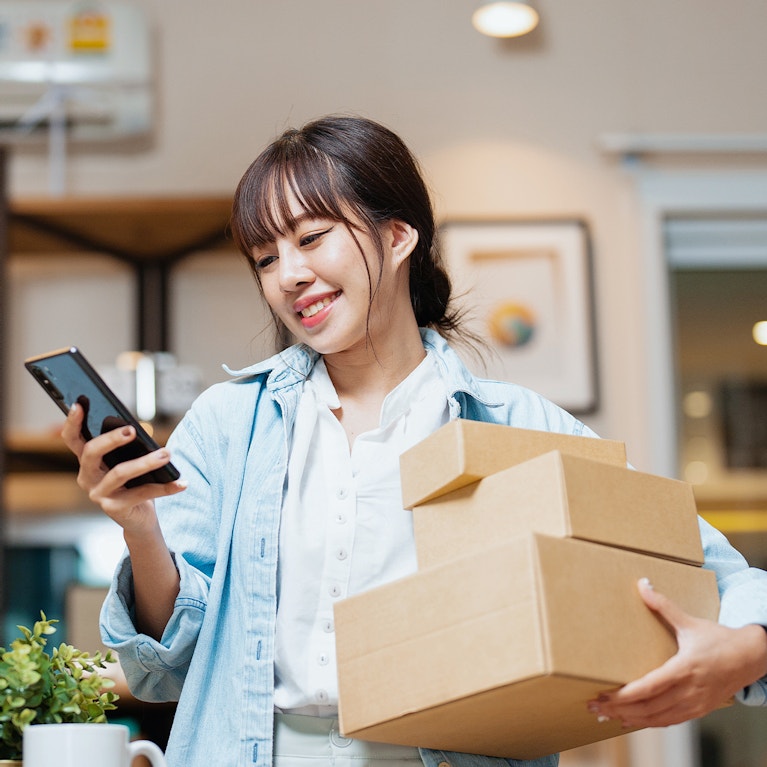 Woman holding packages and smiling at her phone