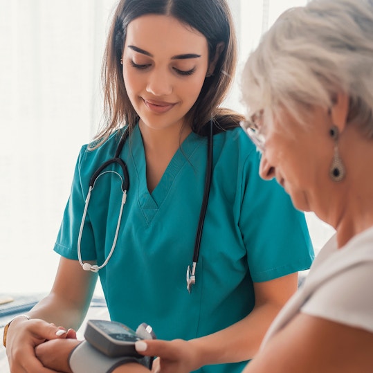 Young nurse measuring blood pressure of elderly woman at home