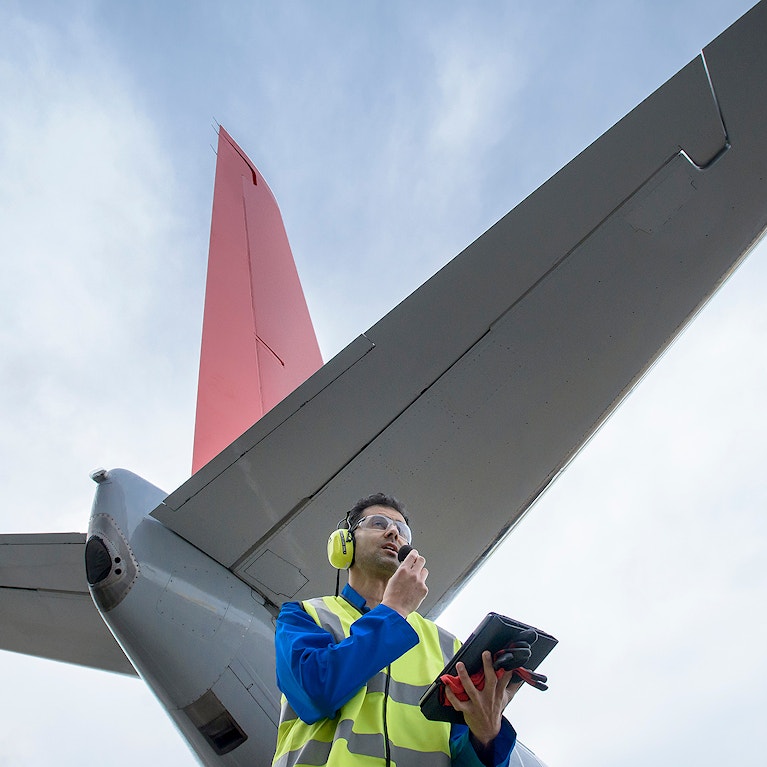 Airside engineer talking on radio near aircraft on runway