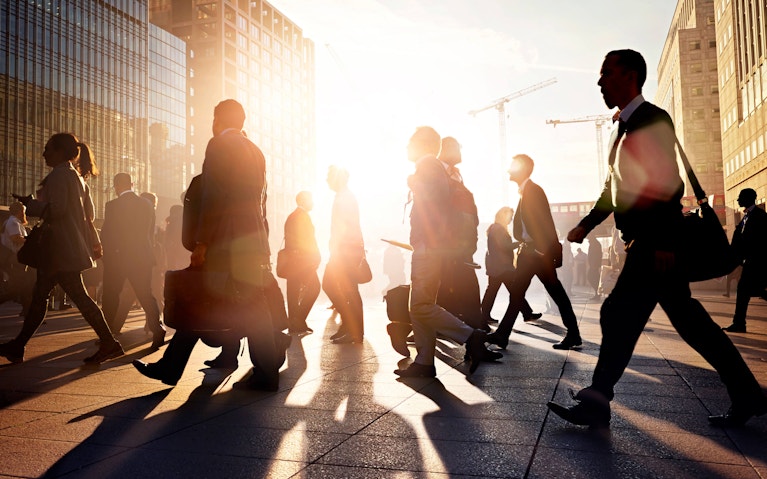 Group of business people walking in city with sun setting behind them