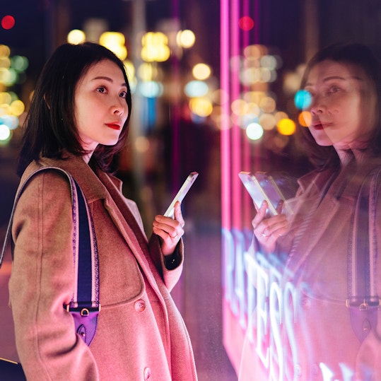 Young woman using smart phone against neon light display on city street at night