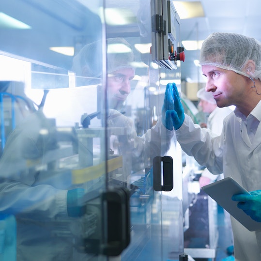 Worker inspecting tablets as they are put into packaging in pharmaceutical factory