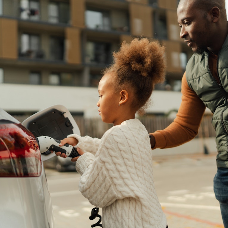 Parent helping child plug EV charger into car in a city environment