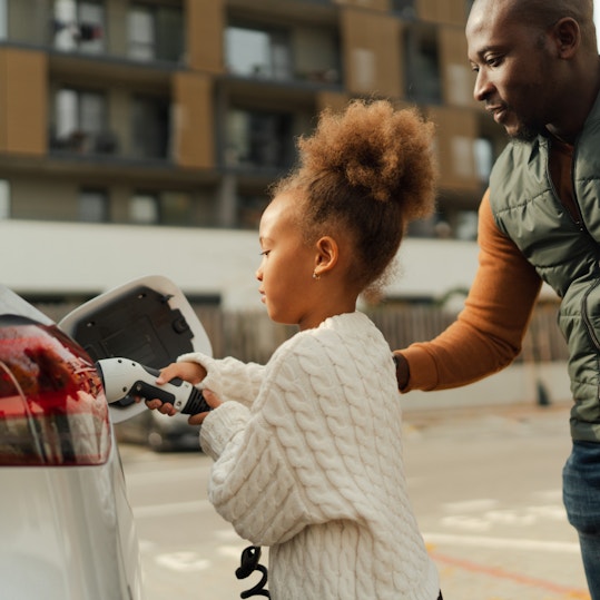 Parent helping child plug EV charger into car in a city environment