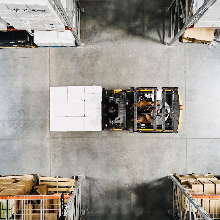 Overhead view of warehouse worker moving pallet of goods with forklift in warehouse