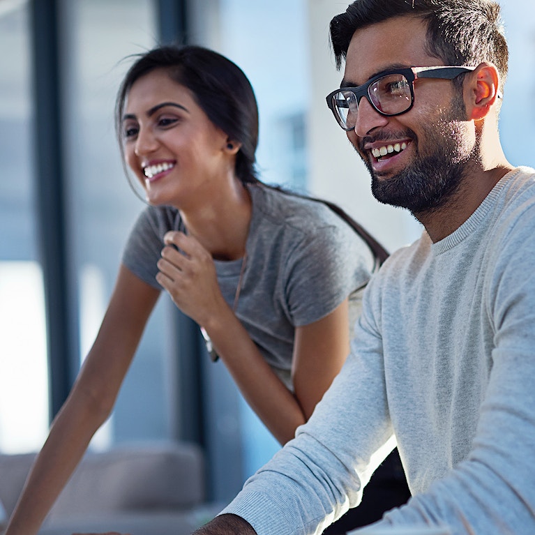 Two young professionals smiling as they look at a computer screen