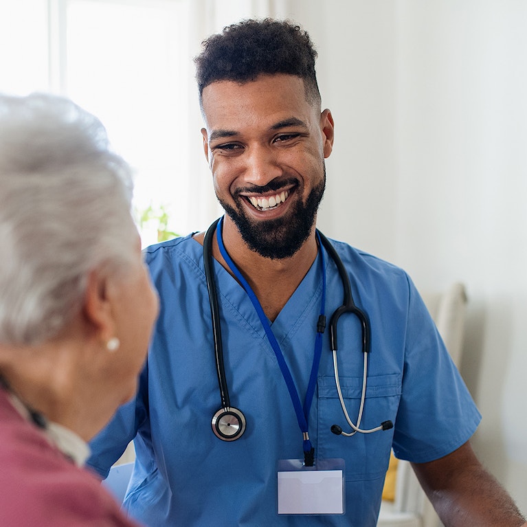 Healthcare worker or caregiver visiting senior woman indoors at home, explaining