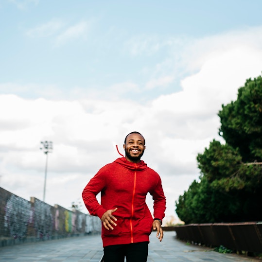 Smiling man in red hoodie running in city