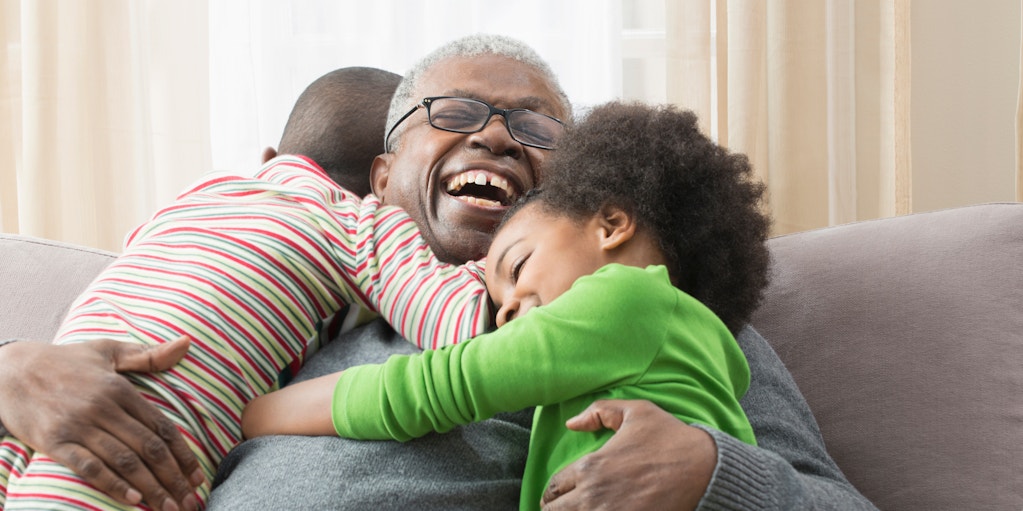 Smiling man sitting on couch, hugging two grandchildren