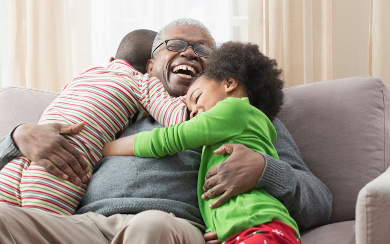 Smiling man sitting on couch, hugging two grandchildren