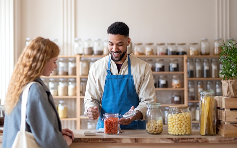 Man shop assistant working in zero waste shop, serving customer